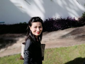 Portrait of smiling woman standing on field against wall