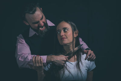 Angry man shouting while holding knife by woman against black background
