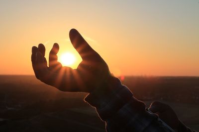 Close-up of silhouette hand against sun during sunset
