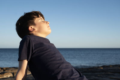 Young kid enjoying on the coast breathing deep fresh sea air with eyes closed