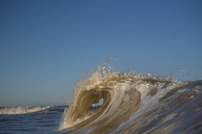 Waves splashing in sea against clear blue sky