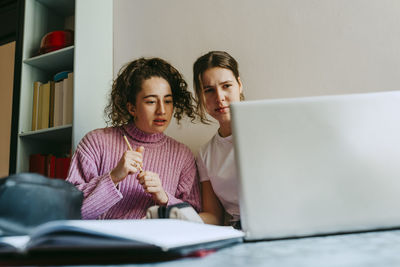 Young female friends looking at laptop while doing homework together