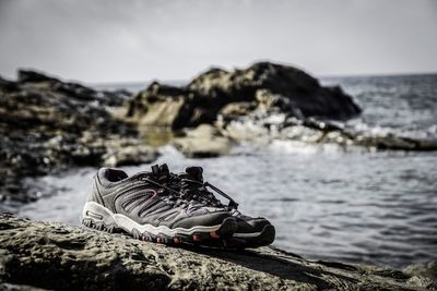 Close-up of shoes on rocks by sea
