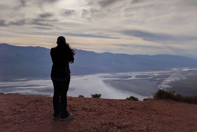 Rear view of woman standing on mountain against sky during sunset