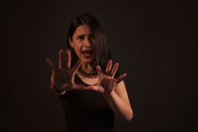 Scared woman gesturing while standing against black background