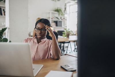 Tensed young businesswoman looking at laptop at desk in office