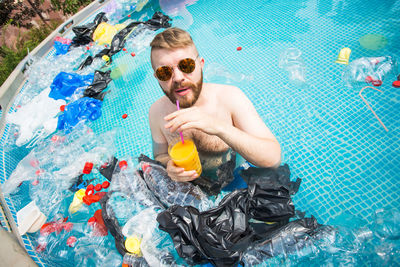 Portrait of man drinking juice in pool with garbage