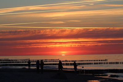 Silhouette people on beach against sky during sunset