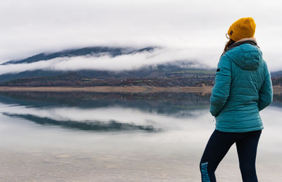 Woman enjoying the view of the lake and the mountains with fog the other side wearing a jacket