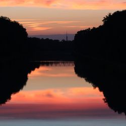 Reflection of silhouette trees in calm lake at sunset