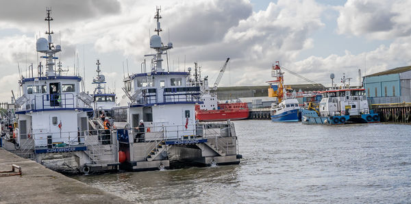 Fishing boats moored at harbor against sky