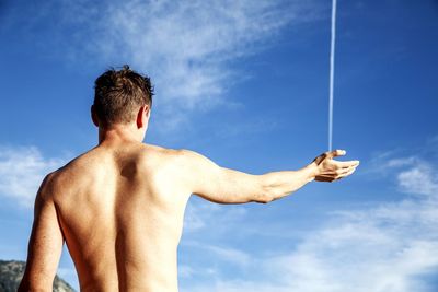 Optical illusion of shirtless man holding vapor trail against blue sky