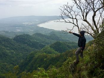 Woman on tree by mountain against sky