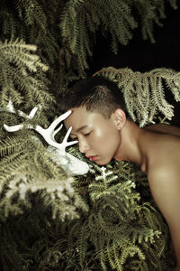 Shirtless man with animal skull leaning on plants