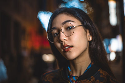 Portrait of young woman standing against illuminated city at night