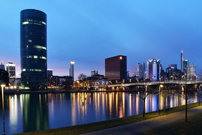 Illuminated city by river against sky at dusk