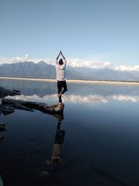 Rear view of man doing yoga by lake