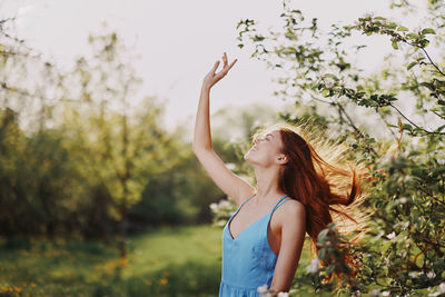 Young woman with arms raised standing against trees