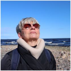 Senior woman wearing sunglasses standing at beach against clear sky