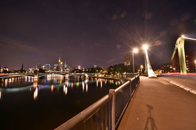 Illuminated city by river against sky at night