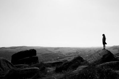 Rear view of woman standing on cliff against clear sky