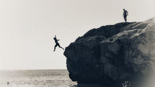 People on rock by sea against clear sky