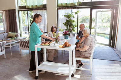 Female caretaker serving breakfast to senior people in nursing home
