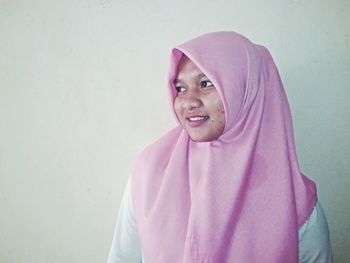 Young woman in pink hijab looking away against white wall