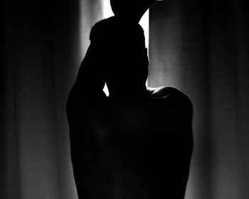 Rear view of a silhouette woman standing against curtain