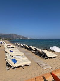 Deck chairs on beach against clear blue sky