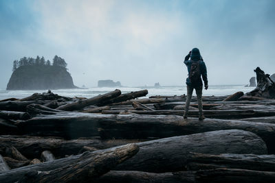 Rear view of woman standing on log against sky