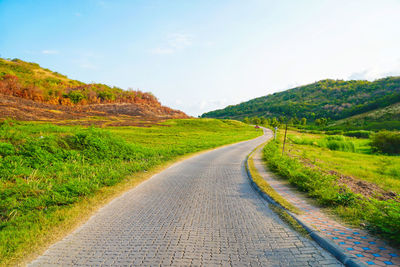 Empty road amidst field against sky