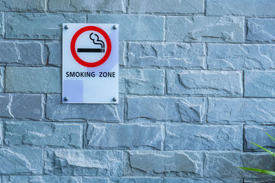 Close-up of smoking zone text on information sign against wall