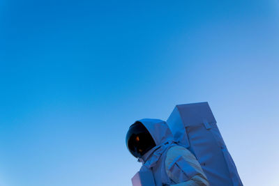 Low angle view of person in astronaut costume against clear blue sky