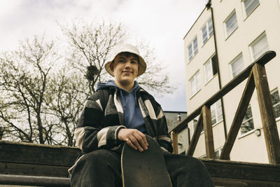 Low angle view of smiling young man wearing bucket hat while sitting on steps