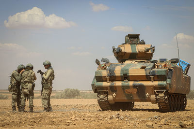 Soldiers discussing while standing by armor tank against sky