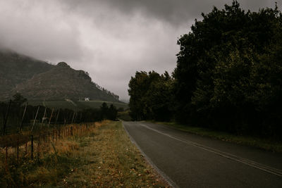 Empty road along trees and plants against sky