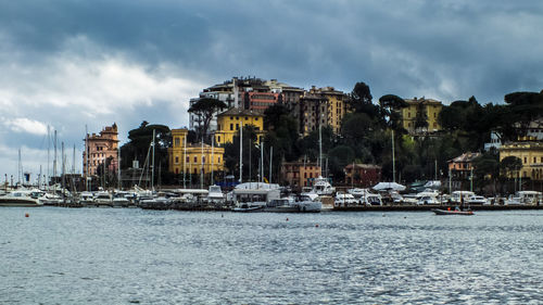 Sailboats in sea by buildings against sky