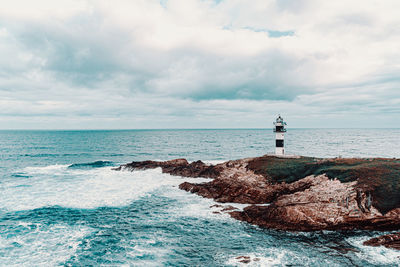 Lighthouse on rocks by sea against sky