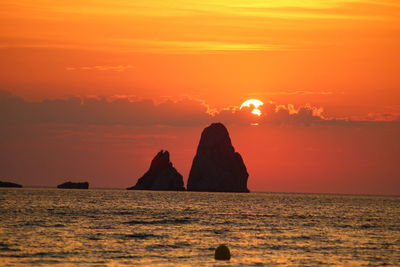 Rock formation in sea against sky during sunset