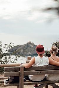 Rear view of couple sitting on bench looking at sea