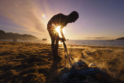 Silhouette man standing at beach against sky during sunset