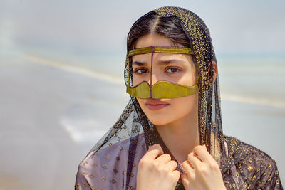 Close-up portrait of young woman wearing traditional clothing standing at beach against sky