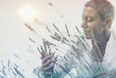 Woman holding plant against sky