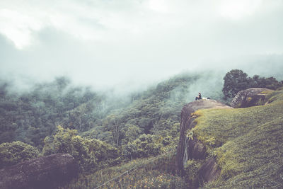 Scenic view of mountains with woman sitting on rock against sky