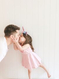 Father kissing daughter against white wall