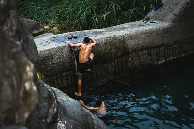 Rear view of shirtless man on rock in lake