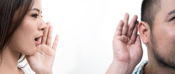 Woman whispering into man ear against white background