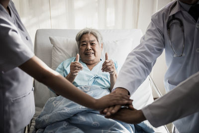 Portrait of female senior patient showing thumbs up signs by doctors stacking hands