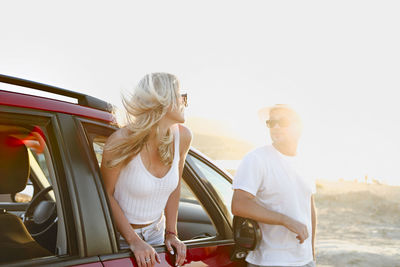 Man standing by woman peeking out from car window against sky